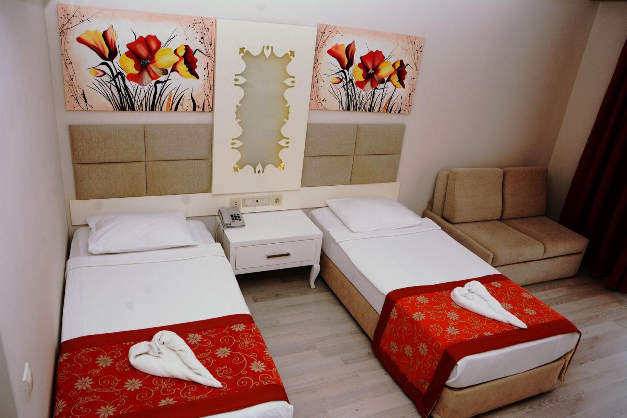 Miramor Hotel & Spa Antalya Bagian luar foto The photo shows a hotel room featuring two single beds with white linens, each adorned with a decorative red throw. The headboards are upholstered in a light beige fabric. Above the beds, there are two large artwork pieces depicting colorful flowers.