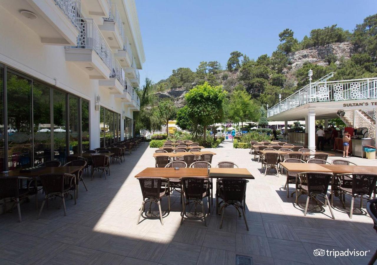 Miramor Hotel & Spa Antalya Bagian luar foto The photo shows an outdoor dining area, likely at a restaurant or cafe. There are several tables with chairs arranged neatly on the paved ground, and some greenery, such as trees and plants, is visible in the background. The setting appears bright an