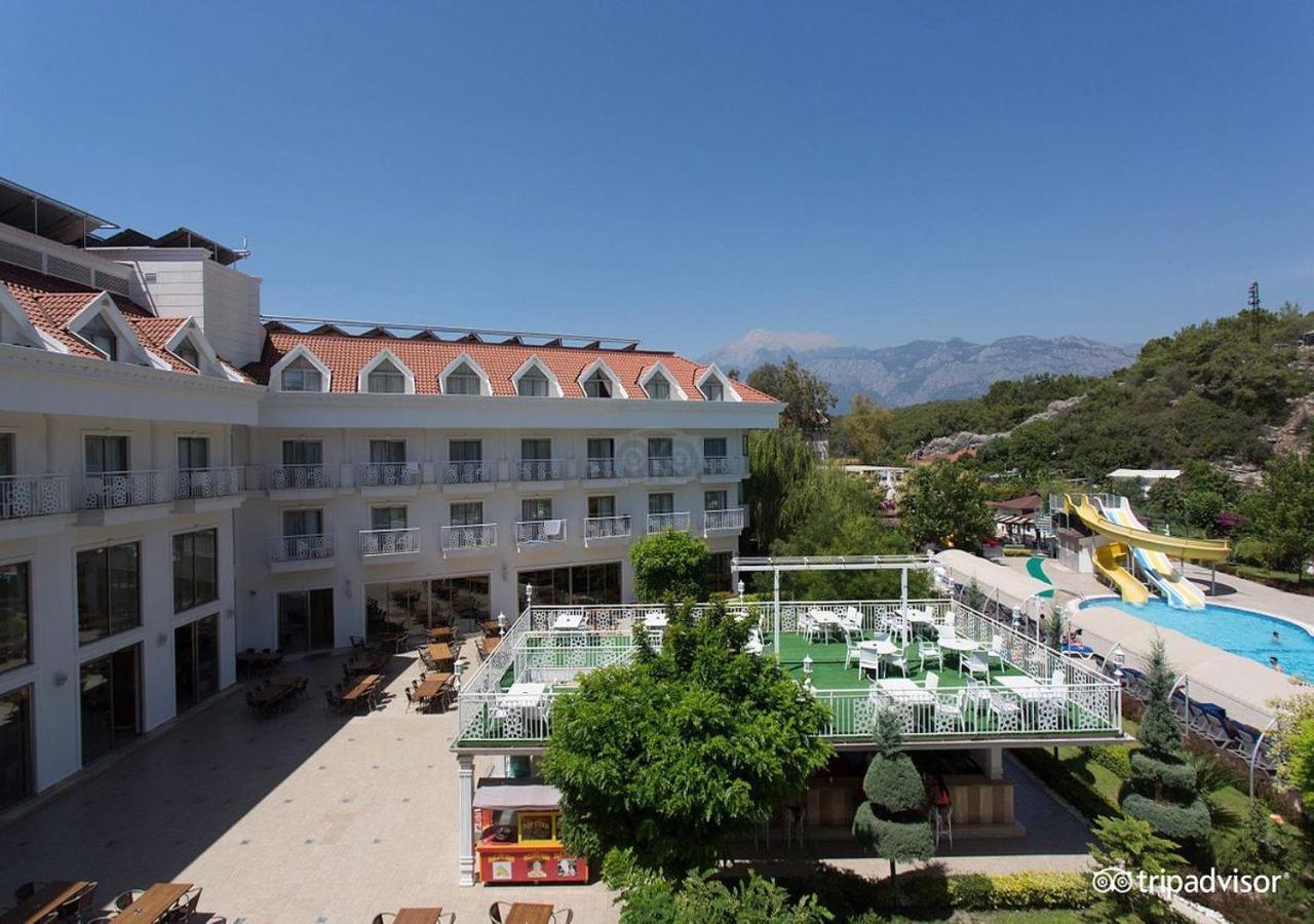 Miramor Hotel & Spa Antalya Bagian luar foto The photo shows a hotel or resort facility with a well-maintained exterior. There is a large green area with grass and some trees, likely intended for relaxation or recreational activities. In the background, there are water slides suggesting an amus